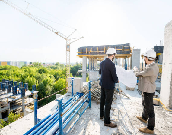 Two engeneers or architects working with house drawings standing together on the structure during the construction process outdoors